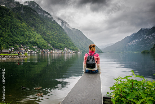 The girl sits on the bridge and looks at the foggy autumn town. Hallstatt, Austria. Girl with a backpack back
