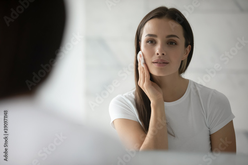Beauty needs care. Pretty young lady doing daily morning skincare procedures, cleansing face skin with natural lotion tonic using cotton disc sponge pad, removing makeup by micellar water at evening