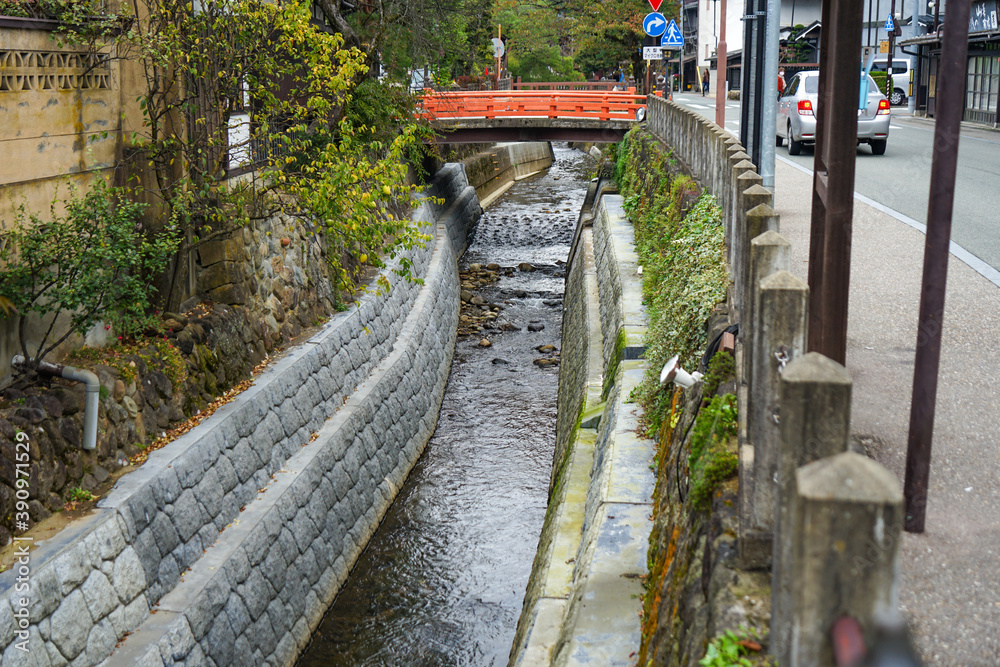 Fototapeta premium 道路の脇を流れる小川と小さな赤い橋