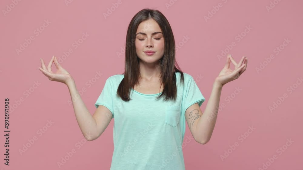 Young brunette woman 20s years old in basic blue t-shirt posing isolated on pastel pink background studio. People lifestyle concept. Hold hands in yoga gesture relaxing meditating trying to calm down Young brunette woman 20s years old in basic blue t-shirt posing isolated on pastel pink background studio. People lifestyle concept. Hold hands in yoga gesture relaxing meditating trying to calm down