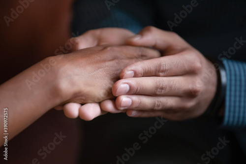 You are not alone. Close up view of male hands holding covering palm of mixed race female expressing care support affection giving hope promising help, biracial family couple reconciling after quarrel