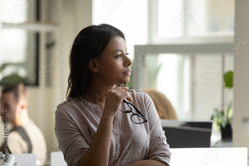 Business vision. Pensive thoughtful millennial biracial female worker employee standing at office workplace taking short break in work looking at distance planning future career, creating new ideas photo
