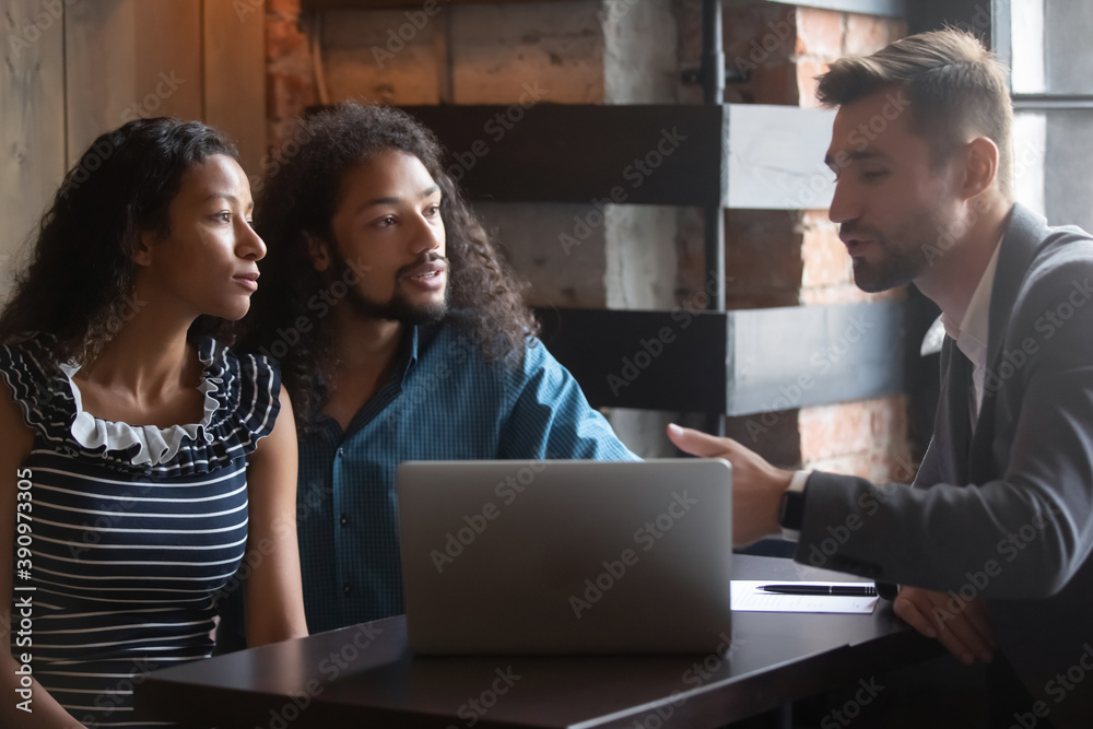Consultation at cafe. Confident male real estate broker, agent, consultant explaining advising young couple clients loan mortgage details, demonstrating project of interior design on laptop screen Consultation at cafe. Confident male real estate broker, agent, consultant explaining advising young couple clients loan mortgage details, demonstrating project of interior design on laptop screen