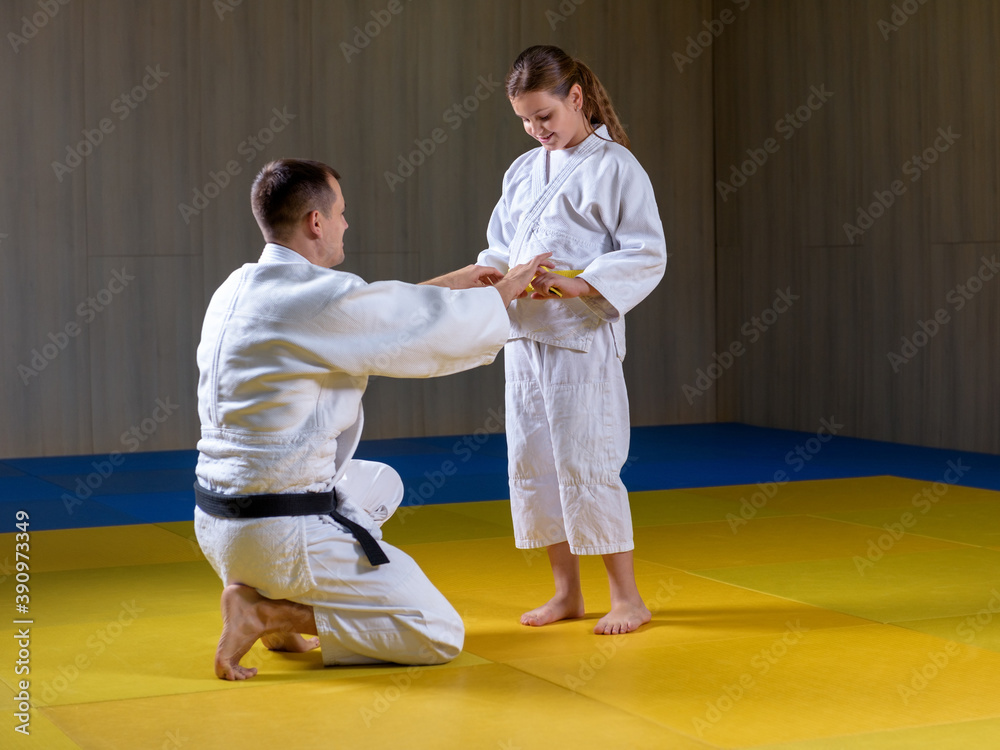 Black belt judoka helps young female yellow belt judoka to tie a belt