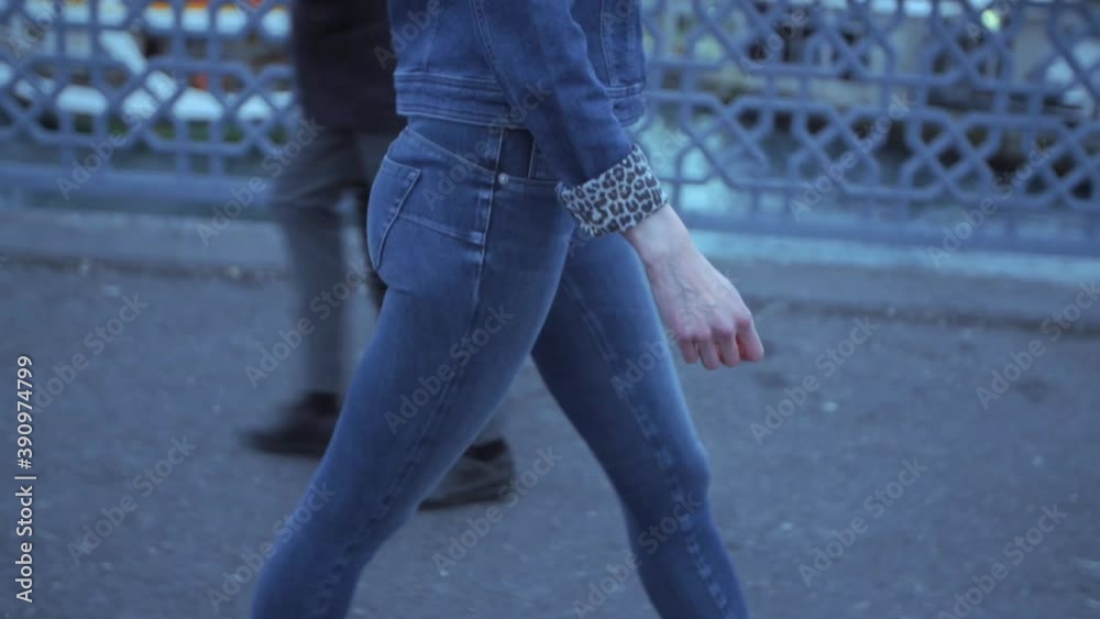 Woman walking down the street, wearing blue jeans and denim jacket with leopard print sleeves. Shot from the side. Woman walking down the street, wearing blue jeans and denim jacket with leopard print sleeves. Shot from the side.