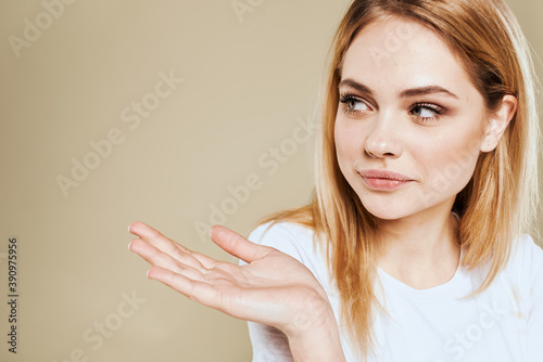 Cheerful woman in a white T-shirt gestures with her hands emotions beige background