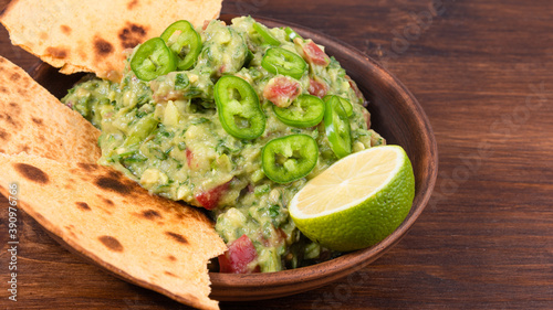Homemade guacamole - a traditional Mexican appetizer of avacado, onion and tomato in a bowl with pieces of toasted tortilla on a rustic wooden table, close-up
