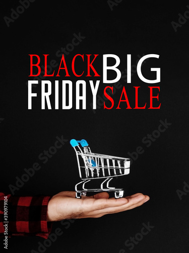 The shopping cart stands on the hand on a black background, concept, sale on Black Friday, advertisement banner, promotion inscription.