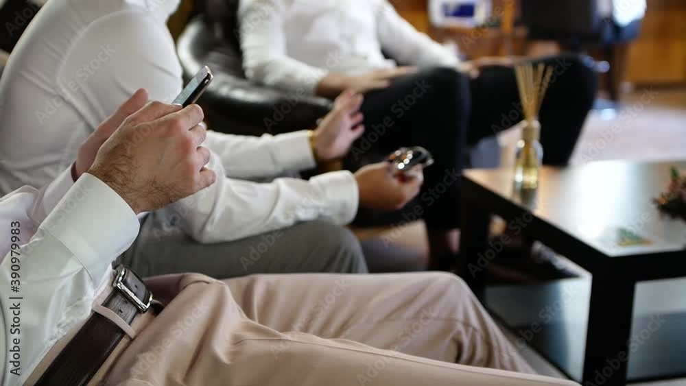 company of young men is sitting on the couch and chatting. Chatting of a group of guys in shirts. Close-up of a young man holding a smartphone in his hands on the background of a company of friends company of young men is sitting on the couch and chatting. Chatting of a group of guys in shirts. Close-up of a young man holding a smartphone in his hands on the background of a company of friends