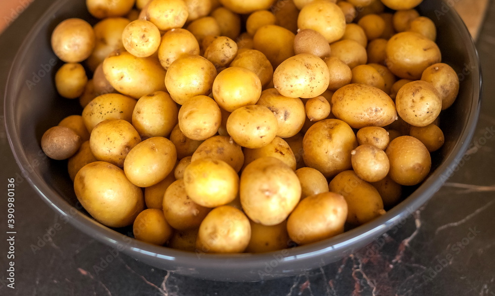 Washed small potatoes in a metal bowl on the background of the table in the kitchen Washed small potatoes in a metal bowl on the background of the table in the kitchen