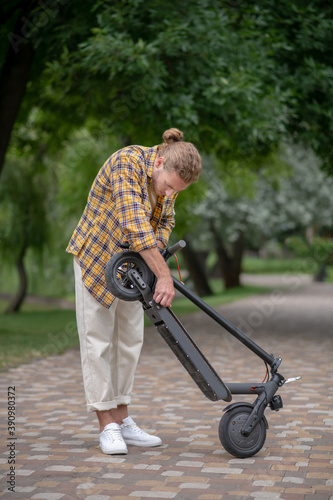 Man in checkered shirt fixing his push scooter