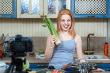 a red-haired girl writes a nutrition vlog and grimaces emotionally. celery in hand