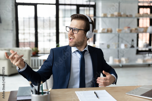 Φωτογραφία Carefree young happy male ceo executive manager listening energetic rock style music in headphones, having fun alone in modern office, pretending playing guitar, enjoying stress free break time