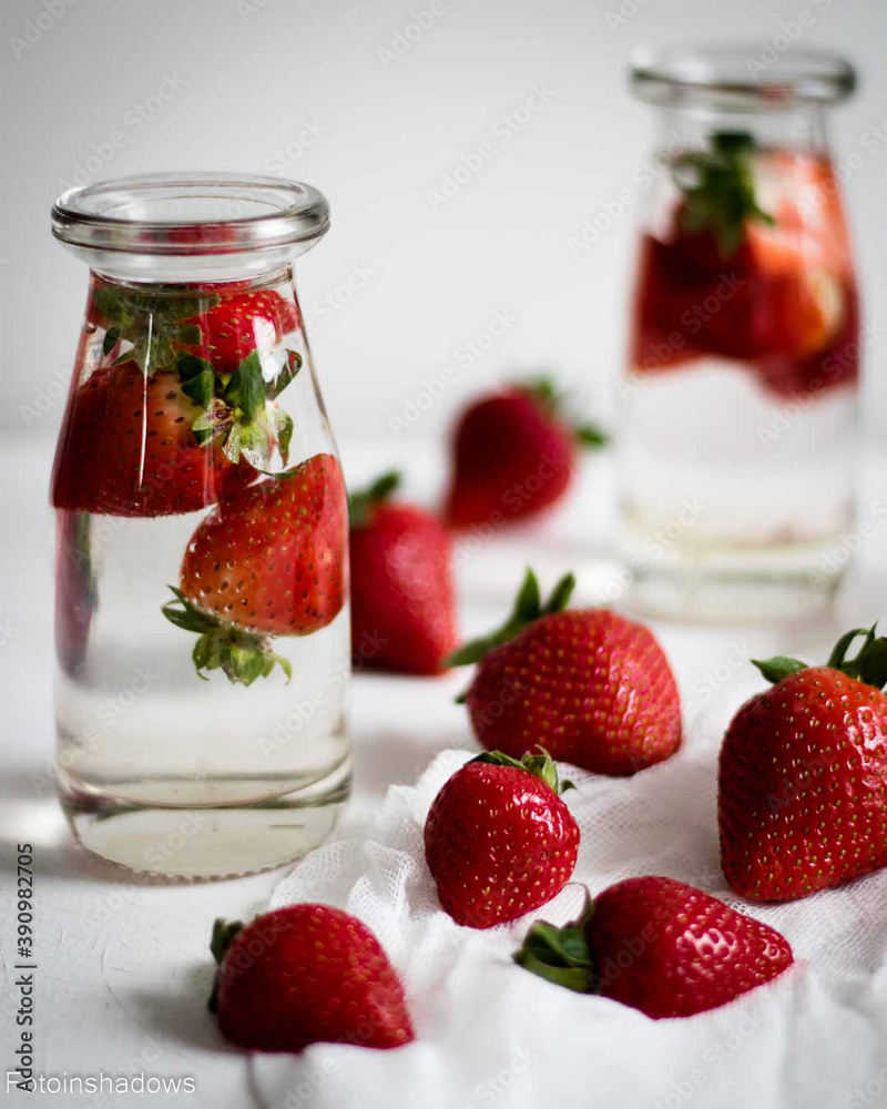 Strawberries in water in glass bottles on a light background Strawberries in water in glass bottles on a light background