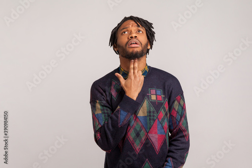 Deeply depressed frustrated african man with dreadlocks holding fingers in gun shape under his head, going to commit suicide, mental problems, crisis. Indoor studio shot isolated on gray background