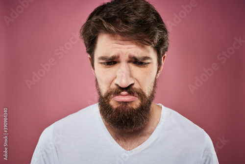 Emotional bearded man in white T-shirt discontent pink background
