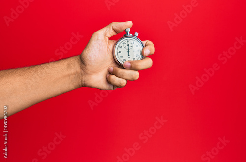 Hand of young hispanic man using stopwatch over isolated red background. photo