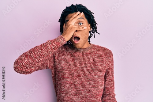 Young african american man wearing casual winter sweater peeking in shock covering face and eyes with hand, looking through fingers afraid © Krakenimages.com