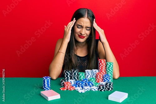 Young hispanic woman sitting on the table playing poker suffering from headache desperate and stressed because pain and migraine. hands on head.