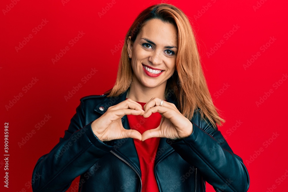 Fototapeta premium Hispanic young woman wearing black leather jacket smiling in love doing heart symbol shape with hands. romantic concept.