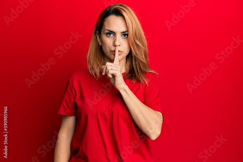 Hispanic young woman wearing casual red t shirt asking to be quiet with finger on lips. silence and secret concept.