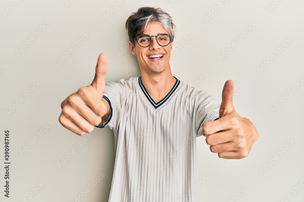 Young hispanic man wearing casual clothes and glasses approving doing positive gesture with hand, thumbs up smiling and happy for success. winner gesture. Young hispanic man wearing casual clothes and glasses approving doing positive gesture with hand, thumbs up smiling and happy for success. winner gesture.