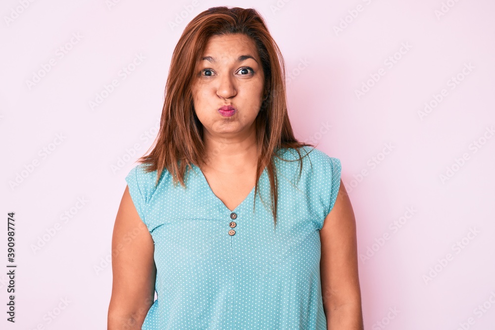 Middle age brunette hispanic woman wearing casual clothes puffing cheeks with funny face. mouth inflated with air, crazy expression. Middle age brunette hispanic woman wearing casual clothes puffing cheeks with funny face. mouth inflated with air, crazy expression.