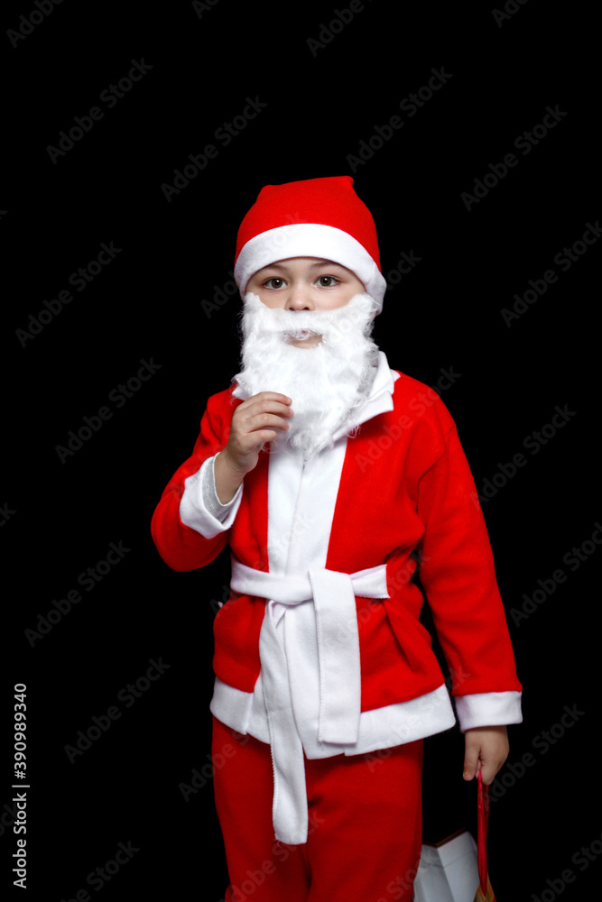 a five-year-old boy in a funny Santa Claus costume stands with a package of gifts. on a black isolated background a five-year-old boy in a funny Santa Claus costume stands with a package of gifts. on a black isolated background