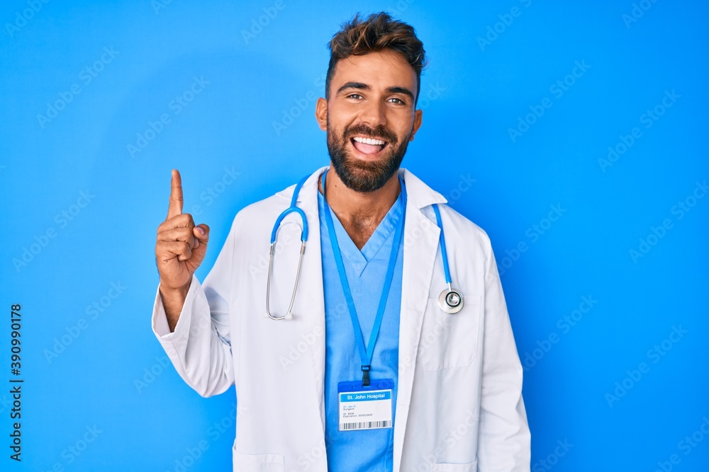 Young hispanic man wearing doctor uniform and stethoscope pointing finger up with successful idea. exited and happy. number one. Young hispanic man wearing doctor uniform and stethoscope pointing finger up with successful idea. exited and happy. number one.