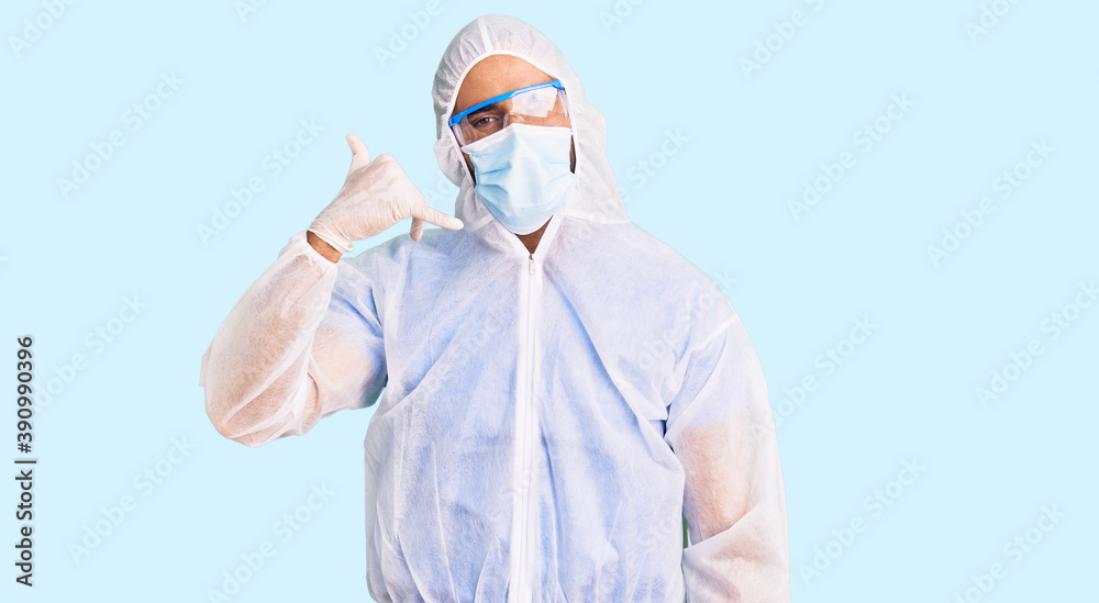 Young hispanic man wearing doctor protection coronavirus uniform and medical mask smiling doing phone gesture with hand and fingers like talking on the telephone. communicating concepts.