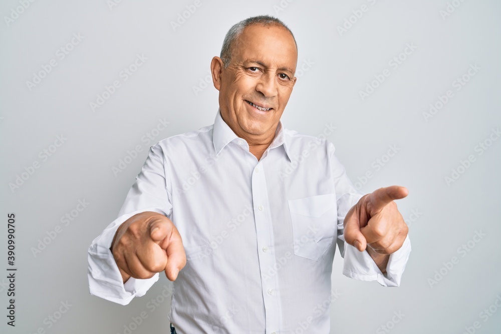 Handsome senior man wearing casual white shirt pointing fingers to camera with happy and funny face. good energy and vibes. Handsome senior man wearing casual white shirt pointing fingers to camera with happy and funny face. good energy and vibes.