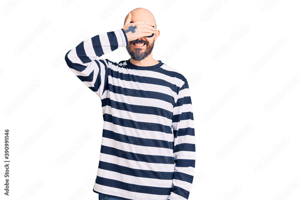 Young handsome man wearing burglar mask smiling and laughing with hand on face covering eyes for surprise. blind concept. Young handsome man wearing burglar mask smiling and laughing with hand on face covering eyes for surprise. blind concept.