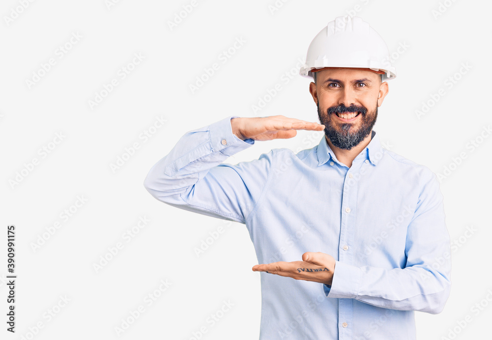 Young handsome man wearing architect hardhat gesturing with hands showing big and large size sign, measure symbol. smiling looking at the camera. measuring concept. Young handsome man wearing architect hardhat gesturing with hands showing big and large size sign, measure symbol. smiling looking at the camera. measuring concept.