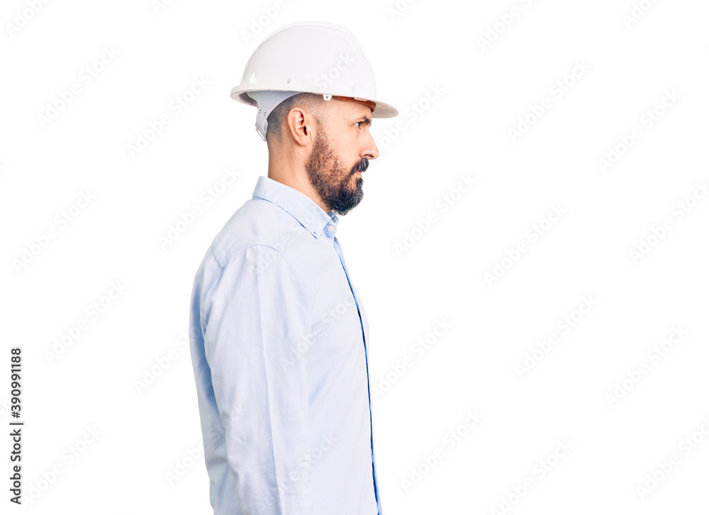 Young handsome man wearing architect hardhat looking to side, relax profile pose with natural face with confident smile.