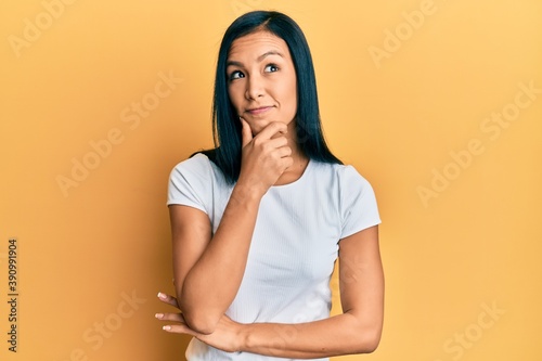 Beautiful hispanic woman wearing casual white tshirt with hand on chin thinking about question, pensive expression. smiling with thoughtful face. doubt concept.