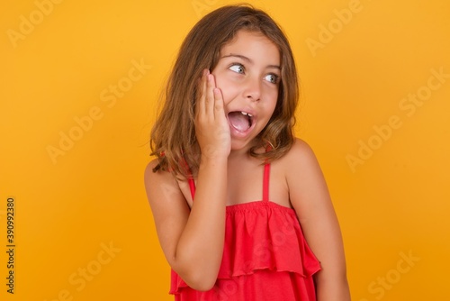 Caucasian young girl standing against yellow background excited looking to the side hand on face. Advertisement and amazement concept.