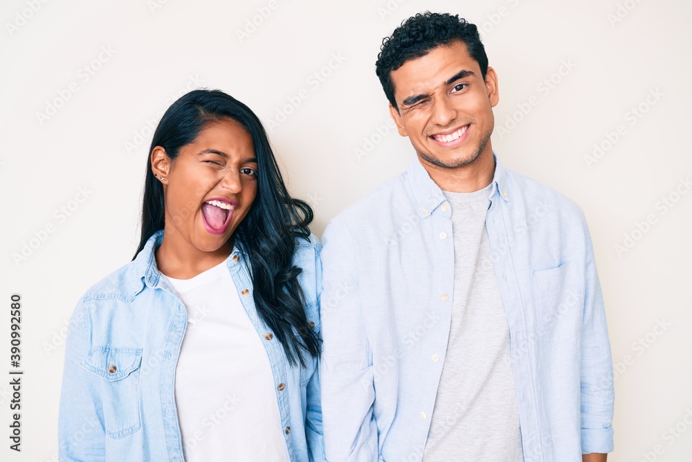 Beautiful latin young couple wearing casual clothes winking looking at the camera with sexy expression, cheerful and happy face. Beautiful latin young couple wearing casual clothes winking looking at the camera with sexy expression, cheerful and happy face.