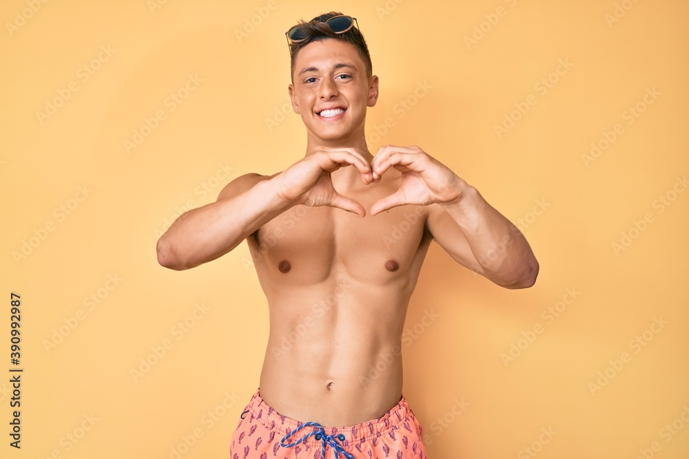 Young hispanic boy wearing swimwear shirtless smiling in love showing heart symbol and shape with hands. romantic concept.