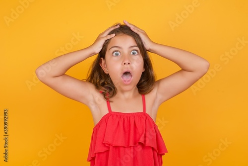Horrible, stress, shock. Portrait emotional crazy young Caucasian girl standing against yellow background clasping head in hands. Emotions, facial expression concept.