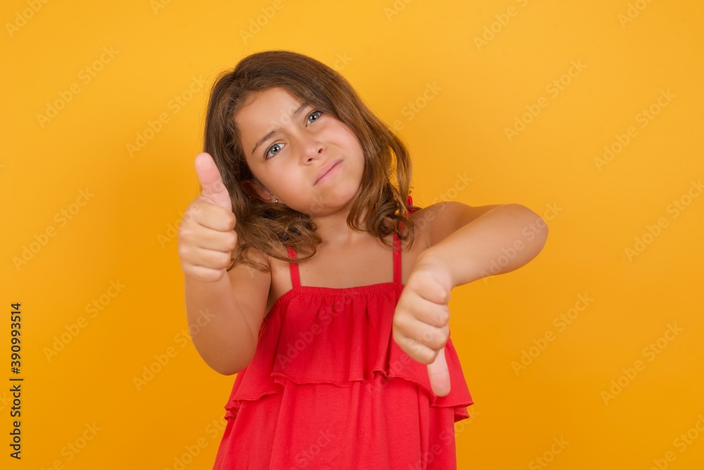 young Caucasian girl standing against yellow background feeling unsure making good bad sign. Displeased and unimpressed. young Caucasian girl standing against yellow background feeling unsure making good bad sign. Displeased and unimpressed.