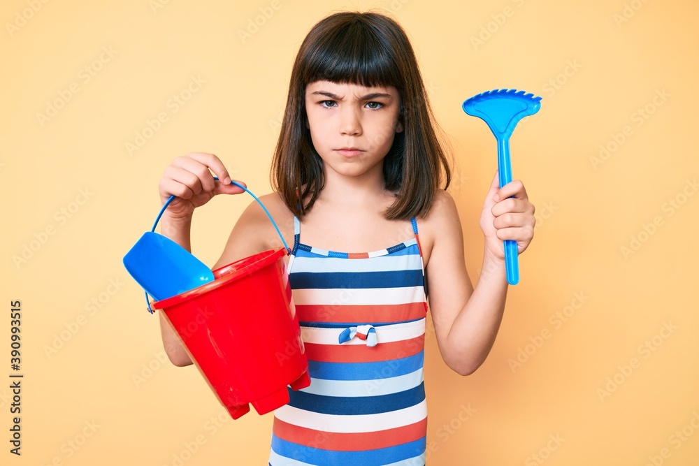 Young little girl with bang playing with summer shovel and bucket toys skeptic and nervous, frowning upset because of problem. negative person. Young little girl with bang playing with summer shovel and bucket toys skeptic and nervous, frowning upset because of problem. negative person.