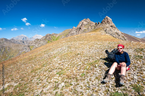 Young trekker woman resting in rocky pass with mountain top in high mountains. Woman with sunglasses sitting next to backpack hiking near Sary Chelek lake Kyrgyzstan, Trekking Central Asia © baisa
