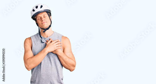 Young handsome man wearing bike helmet smiling with hands on chest with closed eyes and grateful gesture on face. health concept.