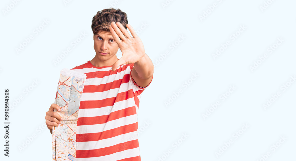 Young handsome man holding city map with open hand doing stop sign with serious and confident expression, defense gesture Young handsome man holding city map with open hand doing stop sign with serious and confident expression, defense gesture