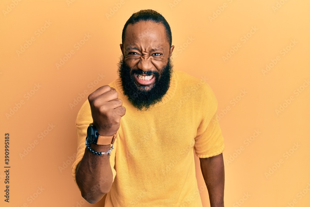 Obraz premium Young african american man wearing casual clothes angry and mad raising fist frustrated and furious while shouting with anger. rage and aggressive concept.