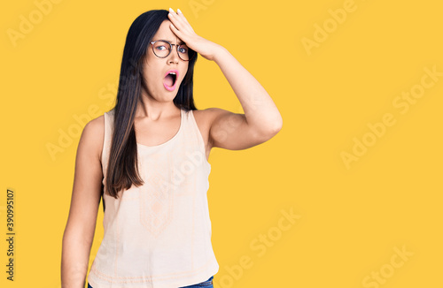 Young beautiful caucasian woman wearing casual clothes and glasses surprised with hand on head for mistake, remember error. forgot, bad memory concept.