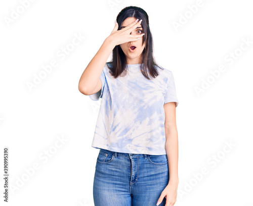 Young beautiful girl wearing casual t shirt peeking in shock covering face and eyes with hand, looking through fingers with embarrassed expression.