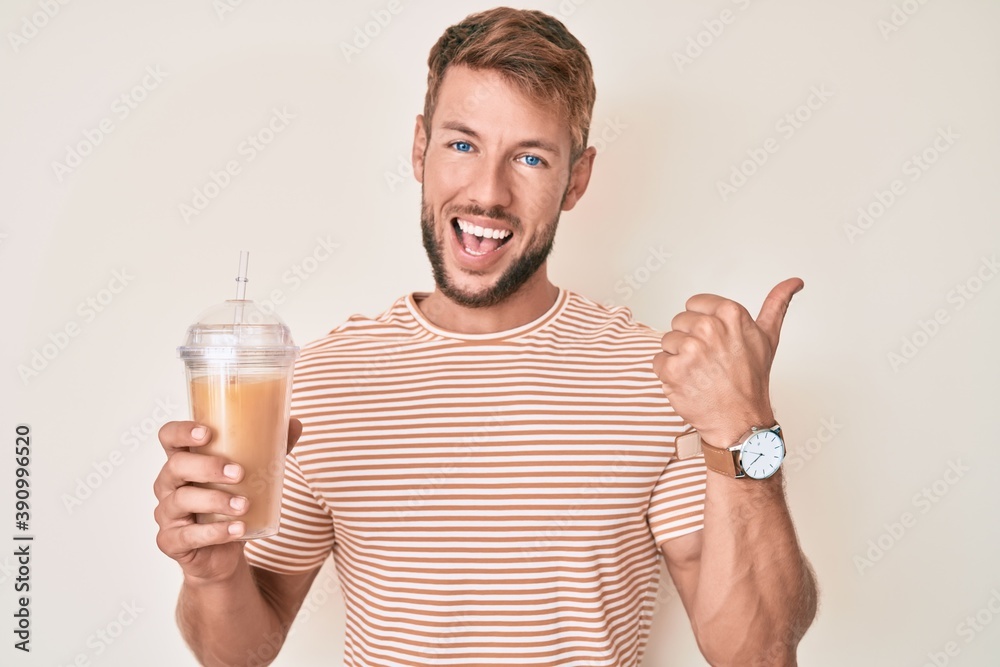 Young caucasian man drinking glass of orange juice pointing thumb up to the side smiling happy with open mouth Young caucasian man drinking glass of orange juice pointing thumb up to the side smiling happy with open mouth