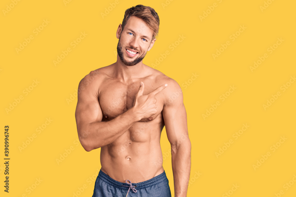 Young caucasian man standing shirtless cheerful with a smile of face pointing with hand and finger up to the side with happy and natural expression on face