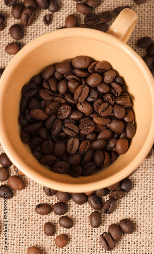 Fototapeta premium yellow coffee cup with grains and raffia cloth background 
